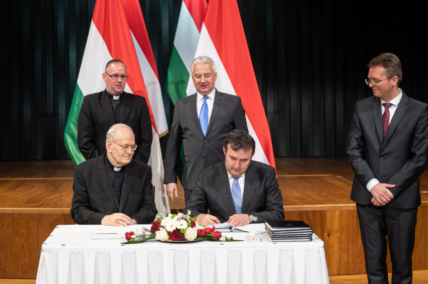 Erdő Péter bíboros, esztergom-budapesti érsek és Palkovics László innovációs és technológiai miniszter aláírja a dokumentumot. Mögöttük Semjén Zsolt miniszterelnök-helyettes és Frankó Tamás Esztergomi Hittudományi Főiskola rektora.